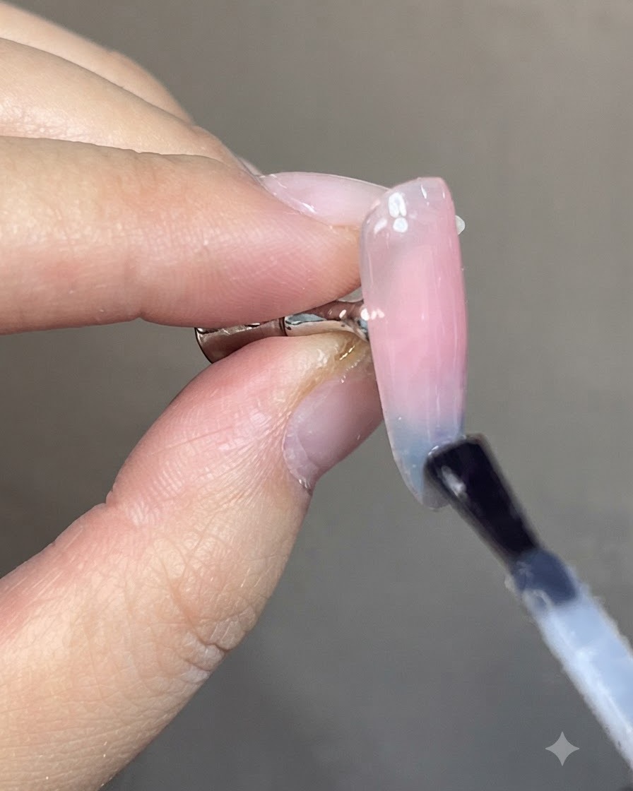 Ein Pinsel trägt einen klaren, glänzenden Überlack auf ein fertiges Nageldesign mit blau-rosa Cat-Eye-Farbverlauf auf.