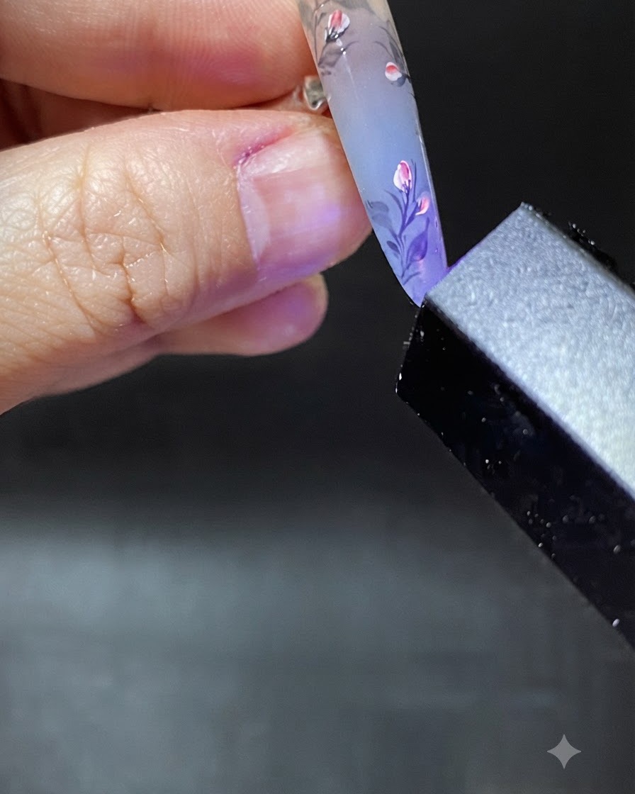 Ein Pinsel trägt einen klaren Tropfen Aufbaugel in der Nähe der Nagelhaut des verzierten Nagels auf.