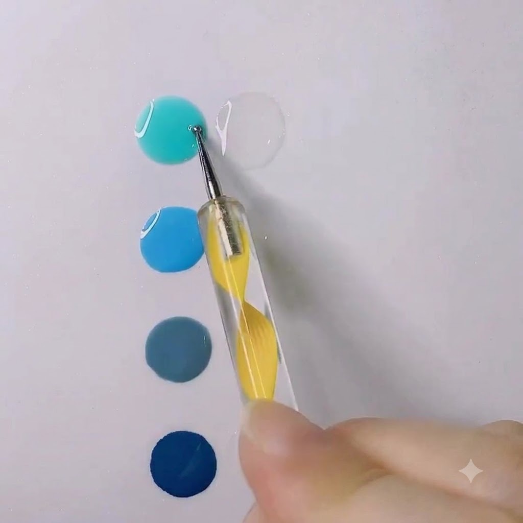 Ein Dotting-Tool rührt einen Tropfen helles, wasserblaues Gel in einen klaren, transparenten Geltropfen auf einer weißen Oberfläche.