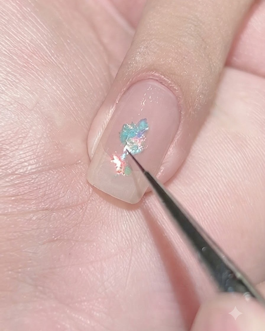 Ein feiner Liner-Pinsel setzt winzige hellblaue Flakes auf einen mit Klarlack versehenen Nagel ab, um ein konzentriertes Cluster zu erzeugen.