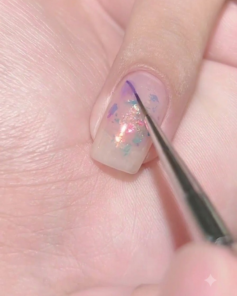 Ein feiner Liner-Pinsel setzt einen winzigen Tropfen dunkelvioletten Gels auf die nassen Oberfläche eines transparent violetten Nagels.