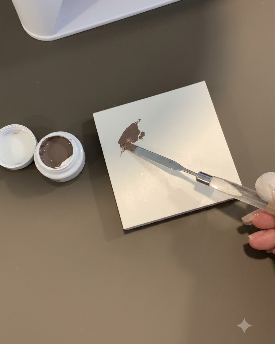 Ein Schwamm-Tool tupft in einen Klecks braungraues Gel auf einer weißen Fliesenoberfläche.