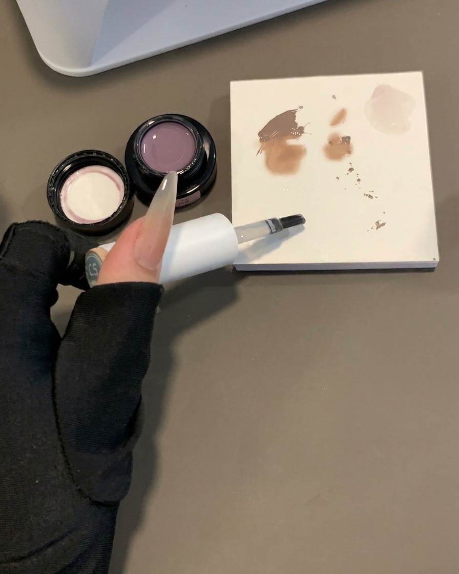 Ein Gelpinsel wird neben einer Mischpalette mit Pigmentmustern in Clear Base-Gel getaucht.