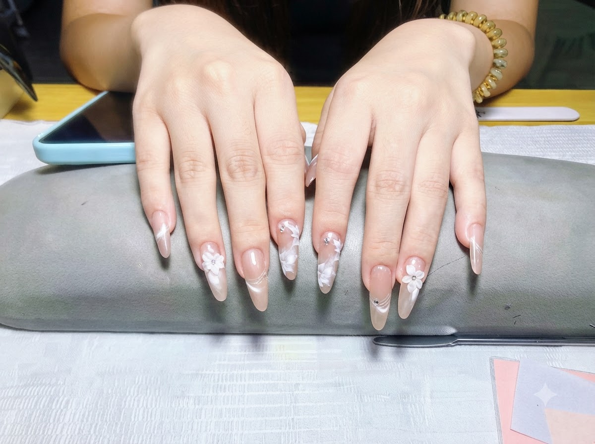 Eine Nahaufnahme konzentriert sich ausschließlich auf die Finger der linken Hand und hebt das Perlmutt-Finish und die weißen Blumenverzierungen hervor.