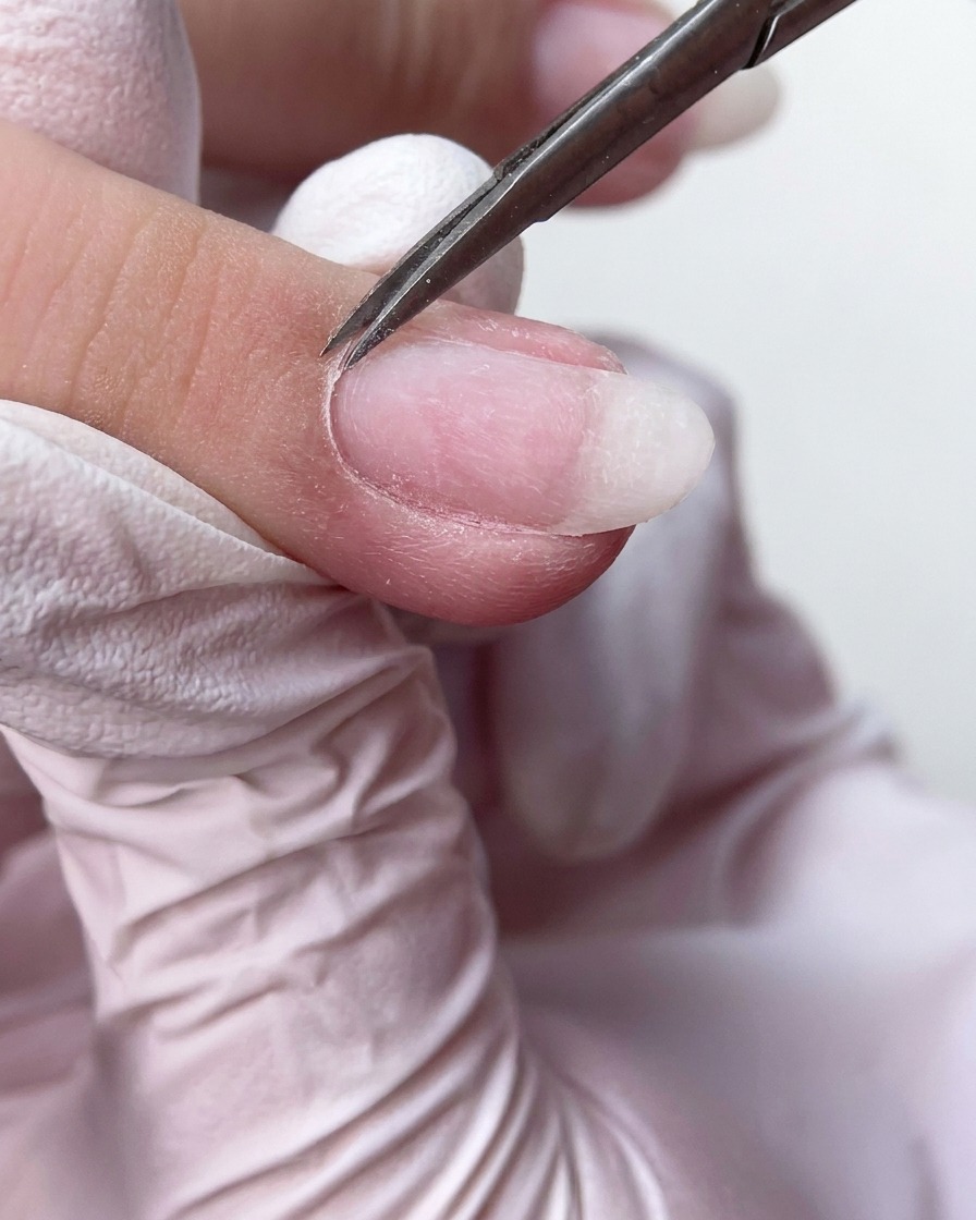 Feine Maniküreschere schneidet überschüssiges, totes Nagelhautgewebe an der Basis des Fingernagels sauber ab.