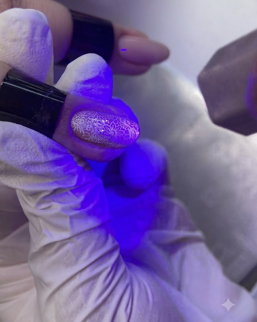 Eine Hand unter einer violetten UV/LED-Nagellampe härtet einen verzierten Fingernagel aus.