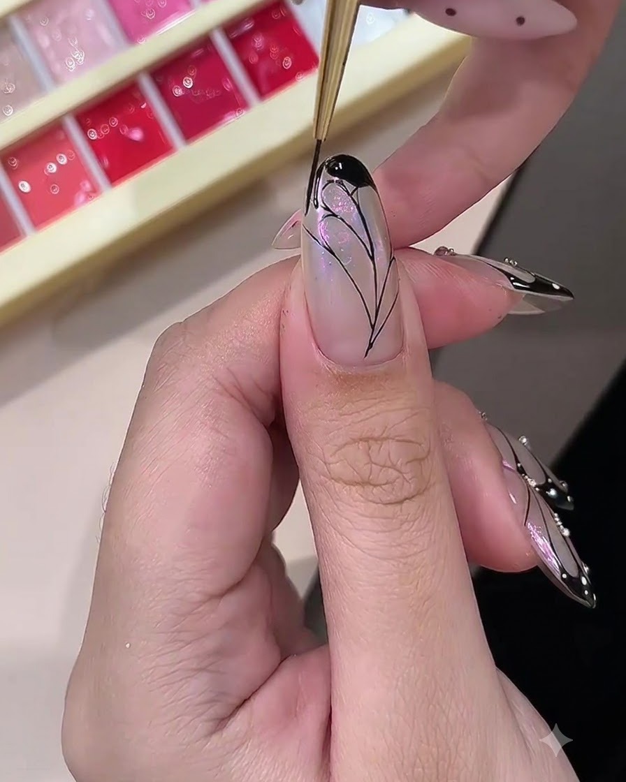 Eine Nageldesignerin füllt die äußeren Ränder eines gemalten Schmetterlingsflügel-Designs mit opakem schwarzem Gel aus.