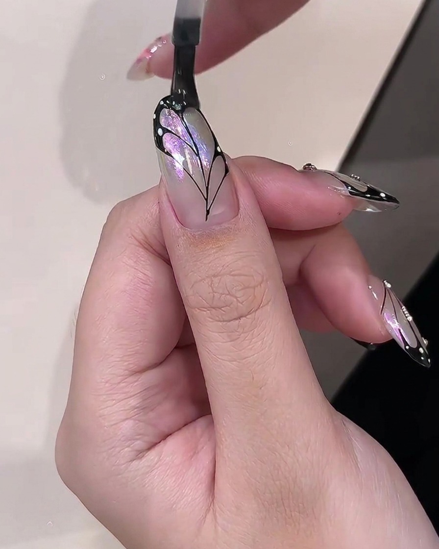 Ein Pinsel trägt einen klaren, glänzenden Top Coat über ein fertiges Schmetterlingsflügel-Nageldesign auf.