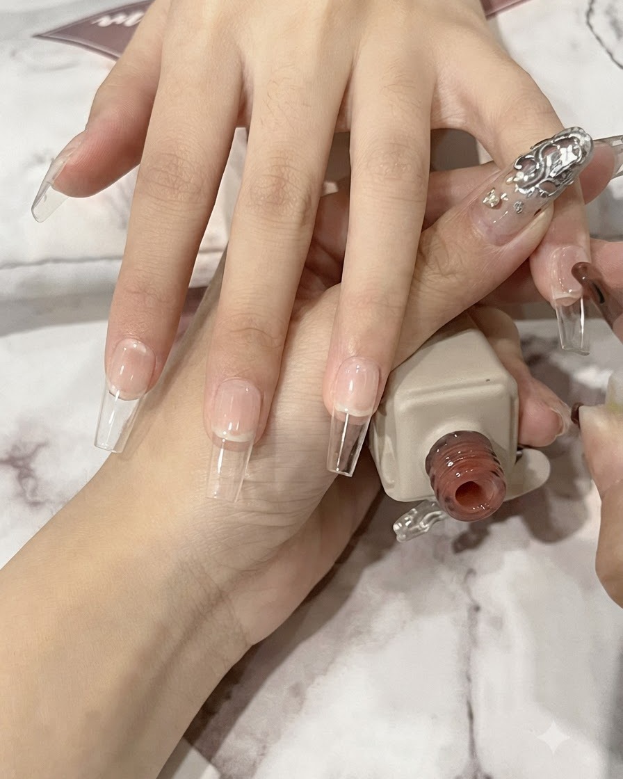 Ein Nagelpinsel trägt eine dünne Schicht durchscheinendes Nude-Gel auf eine lange sargförmige natürliche Nagelplatte auf.