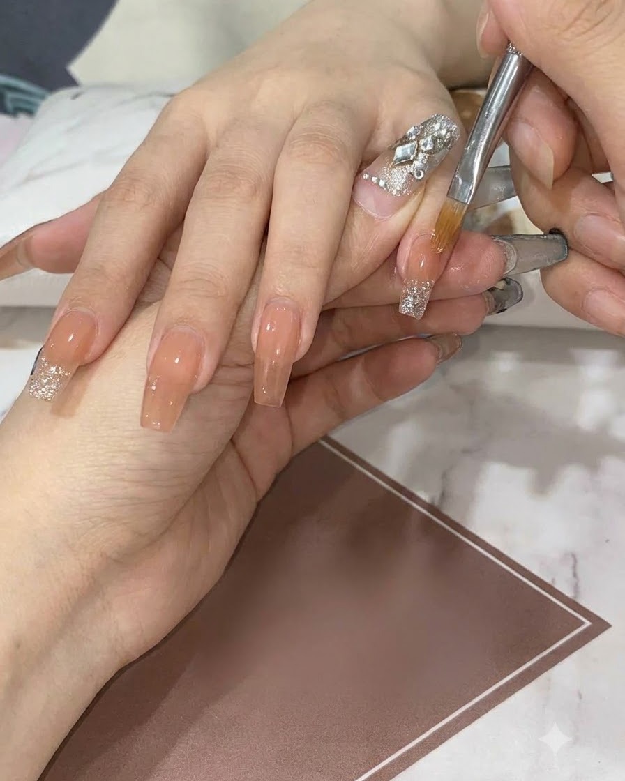 Ein flacher Detailpinsel zieht und verblendet Silberglitter auf einem Nude-Nagel nach unten, um einen sanften Farbverlauf zu erzeugen.