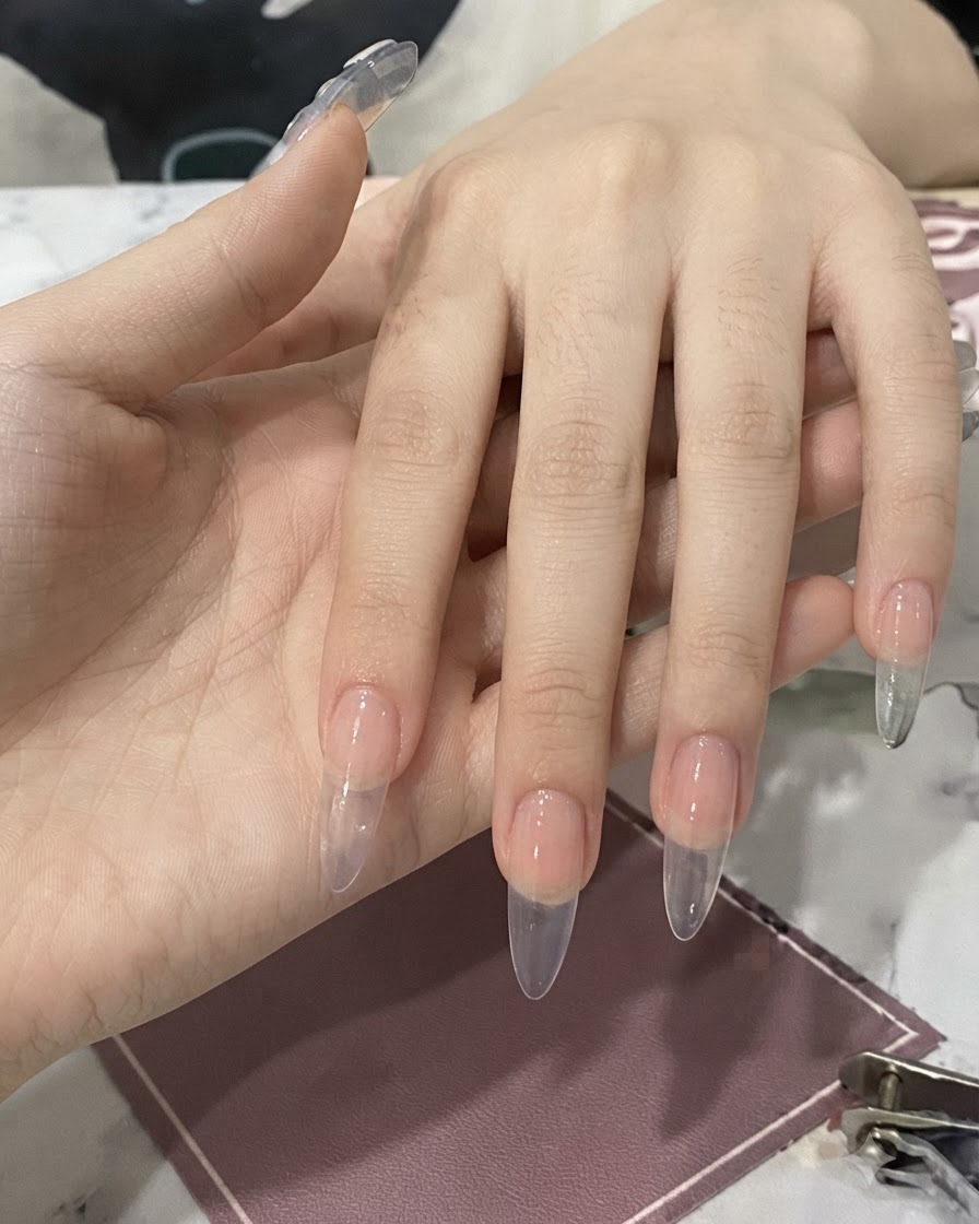 Eine Hand hält eine Flasche mit Pinsel, der klaren Nagelkleber auf einen vorbereiteten Fingernagel aufträgt.