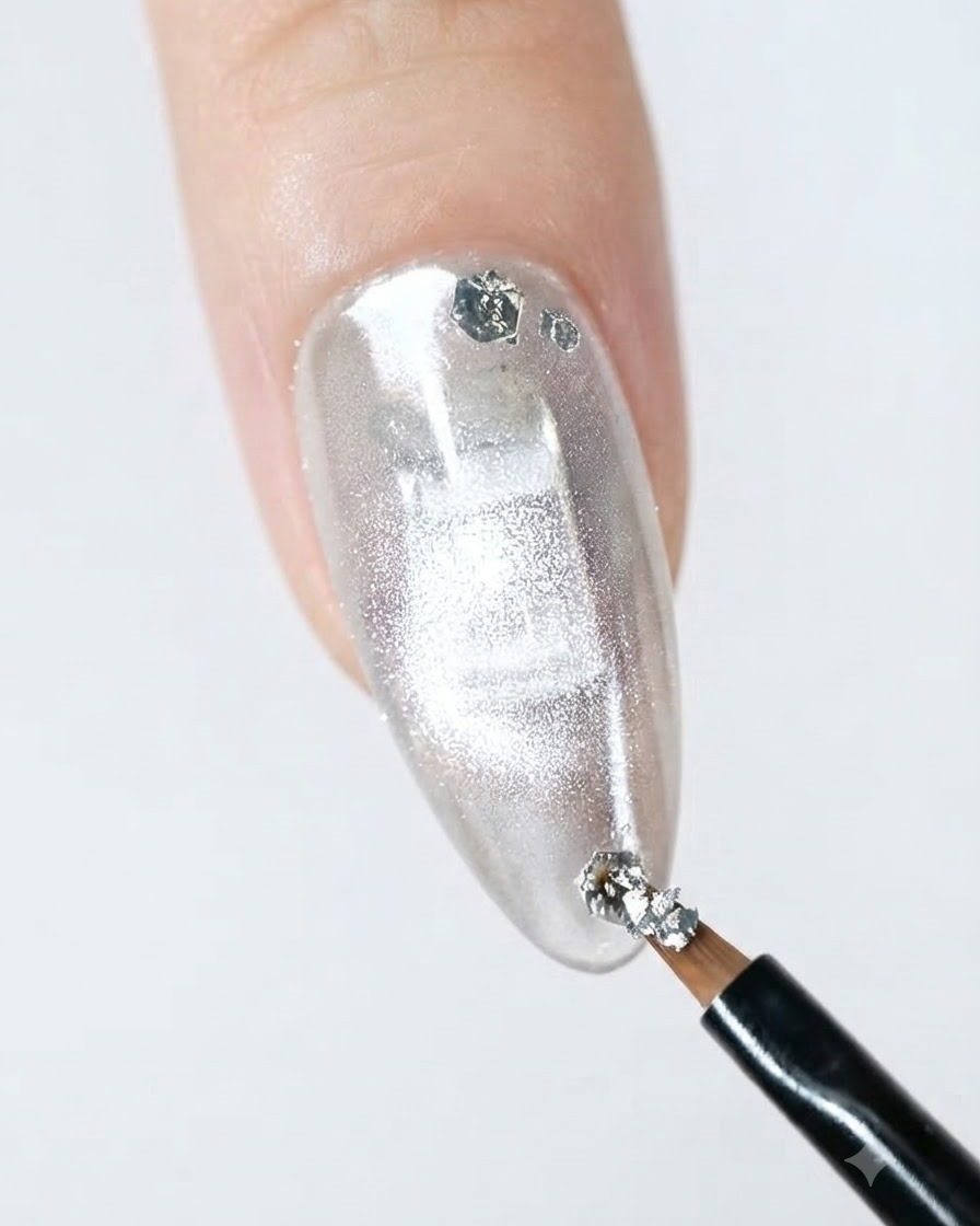 Ein feiner Liner-Pinsel trägt silberne Glitzerflocken auf den Rand eines fertigen Nagels auf.