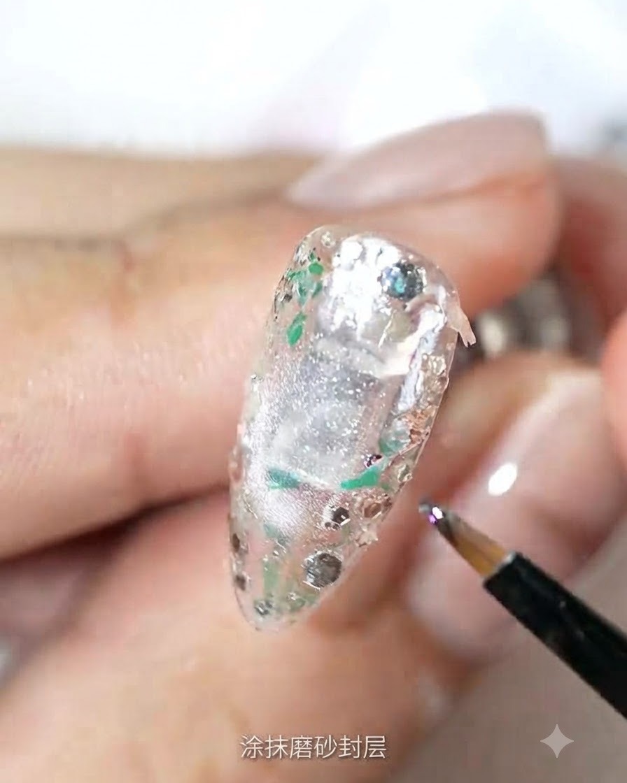 Ein feiner Pinsel trägt matten Top Coat über eine strukturierte, mit Glitzer versehene Nageloberfläche auf.