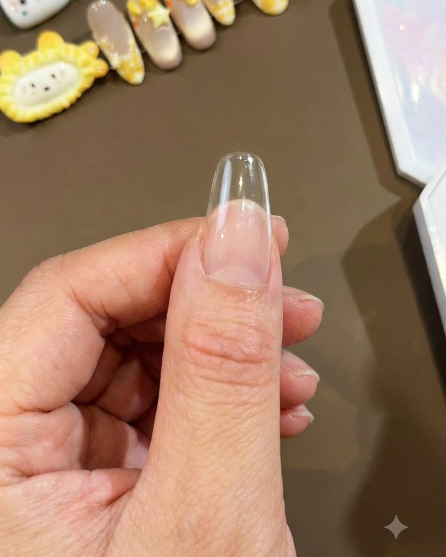 Eine Nahaufnahme eines klaren, langen Mandel-Nageltips, der gegen einen Daumen gehalten wird und bereit für die Nail-Art-Anwendung ist.