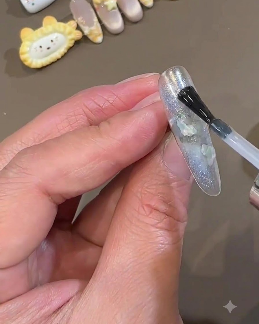 Ein Nagellackpinsel trägt eine glatte Schicht klaren Top Coat über einen versiegelten eisblauen Press-On-Nagel auf.