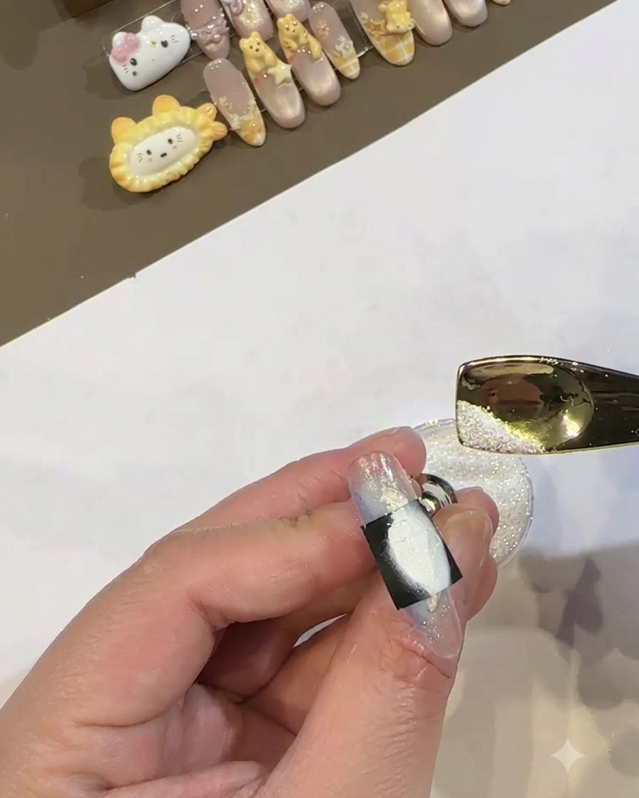 Ein kleiner metallener Löffel gießt schimmerndes weißes Pulver über den nassen, weißen Gelbereich, der von einer schwarzen Schablone auf einem Nagel eingerahmt wird.