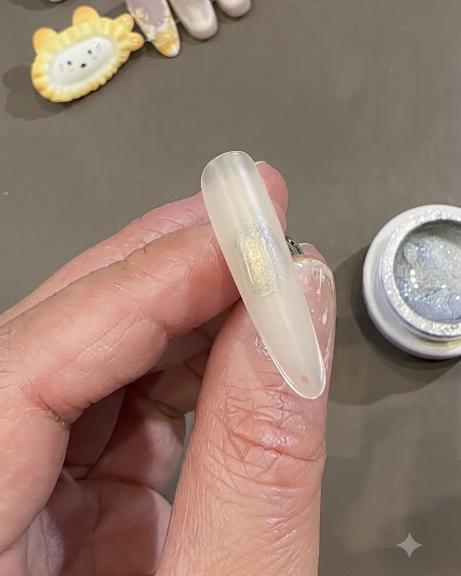Eine Nahaufnahme einer Hand, die eine vorbereitete, gefrostete Nagelspitze mit einem rechteckigen Pflaster aus klarem Slip-Gel in der Mitte hält.