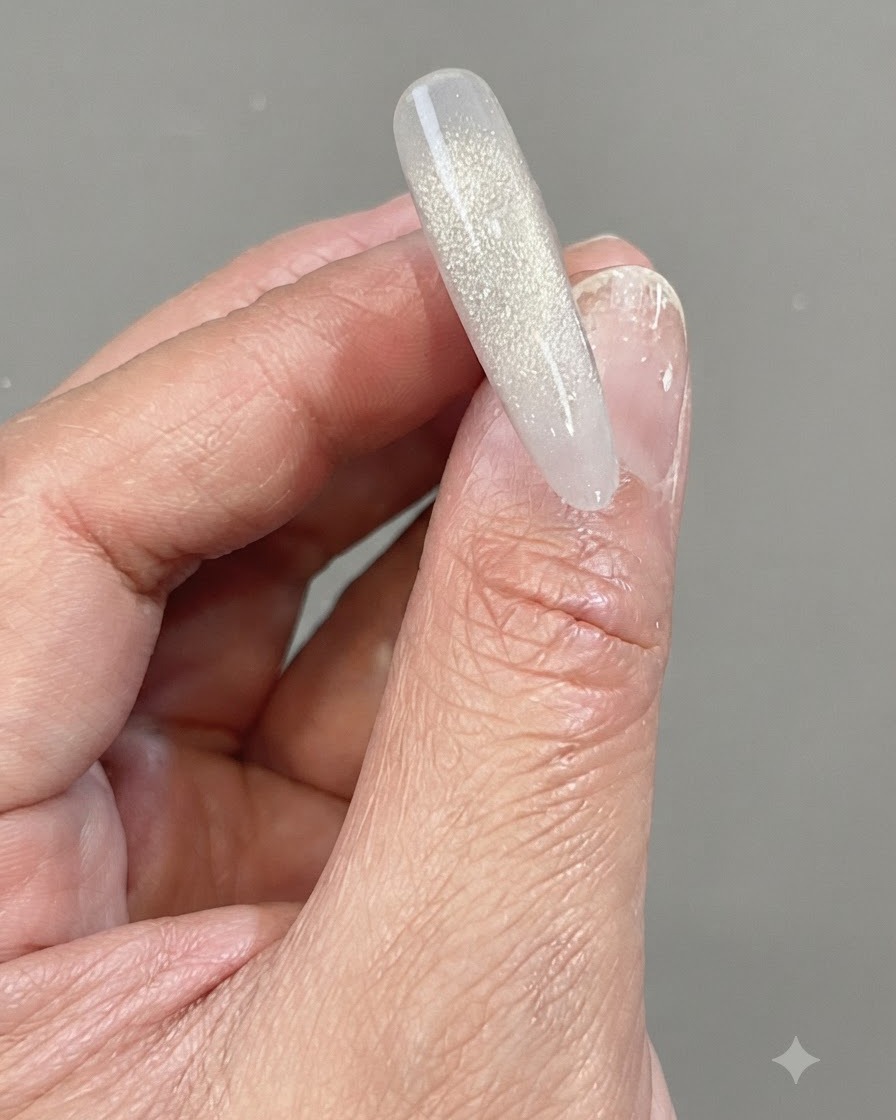 Eine Hand hält eine klare Nagelspitze mit einem schimmernden, vertikalen Farbverlauf aus reflektierendem Shattered-Diamond-Gel.