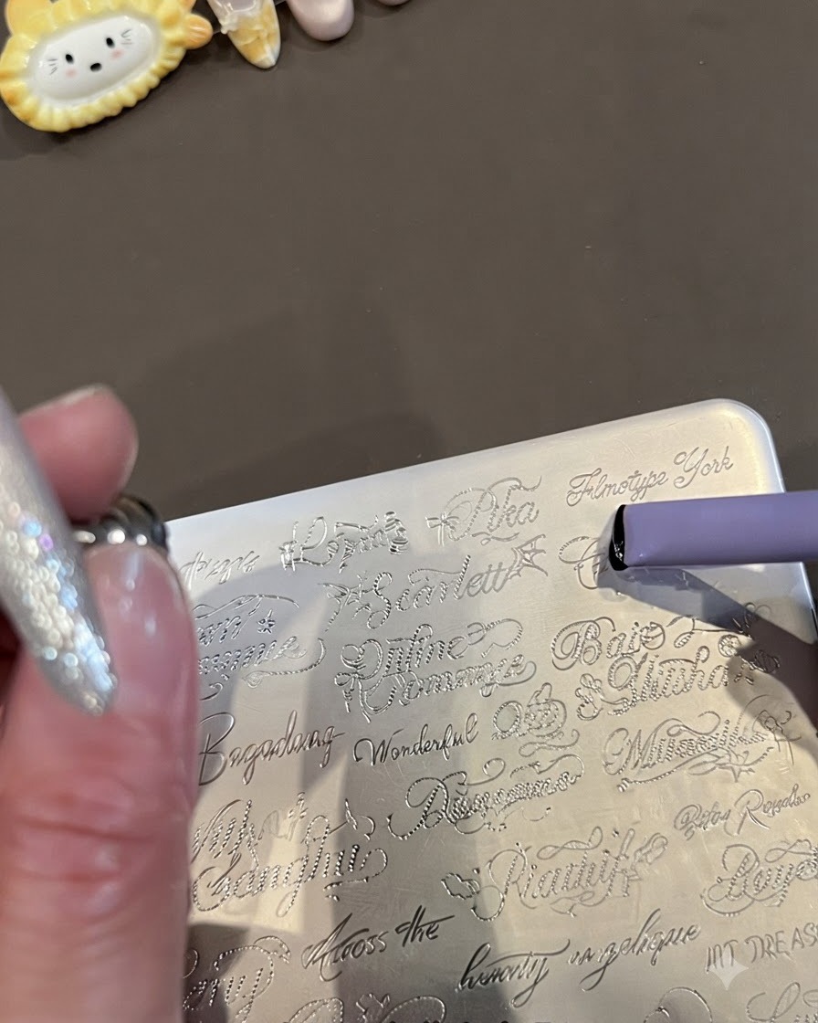 Eine Nahaufnahme einer Metall-Stamping-Platte, die gravierte kursive englische Wörter und einen lila Jelly-Stamper zeigt, der das Design aufnimmt.