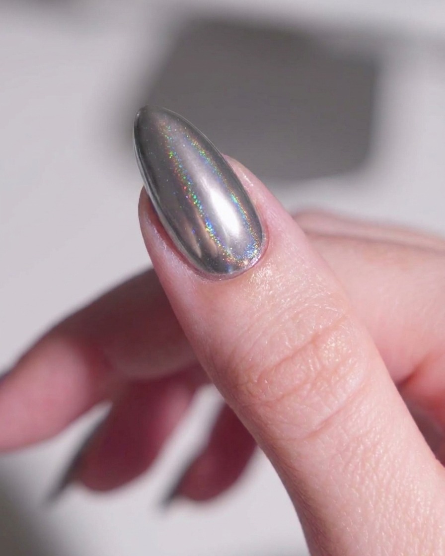 Ein weicher Make-up-Pinsel fegt sanft loses, metallisch silbernes Puder von der Haut um einen mandelförmigen Chrom-Nagel.