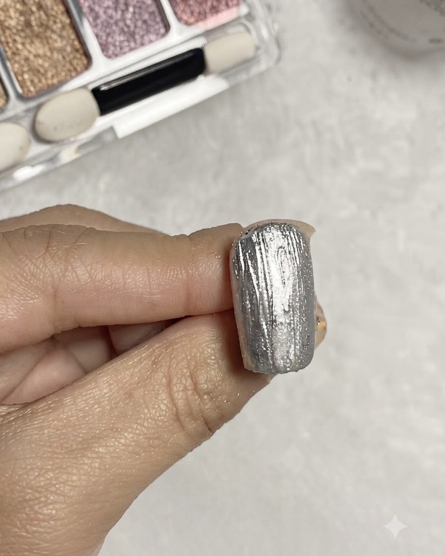 Ein Pinsel trägt klaren Base-Gel über eine strukturierte silberne Metallic-Nageloberfläche auf.