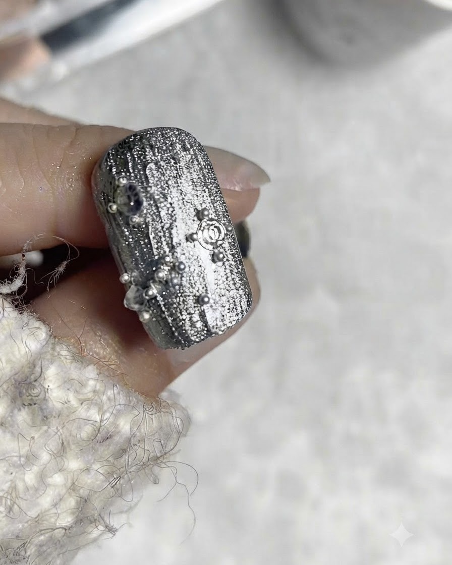 Ein Nageldesign zeigt eine quadratisch geformte Stahlperle, die zentral mit umgebenden winzigen Stahlperlen platziert wurde.