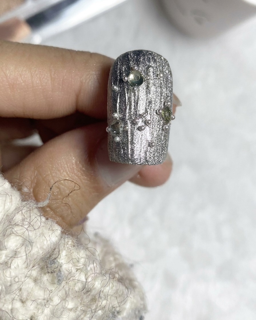 Ein Top-Coat-Pinsel vollendet ein verziertes, silbernes, strukturiertes Nageldesign.