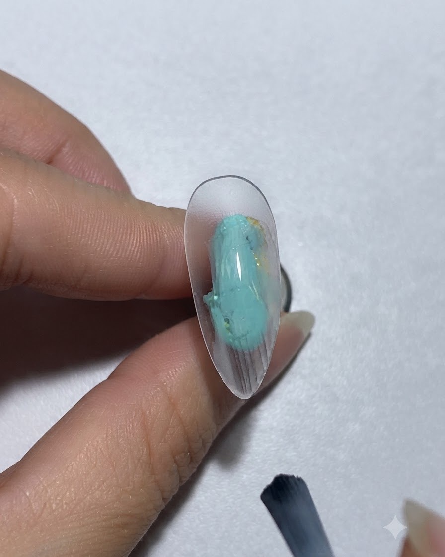Ein Pinsel trägt grünlich-blaues Farbgel auf einen Nagel auf.