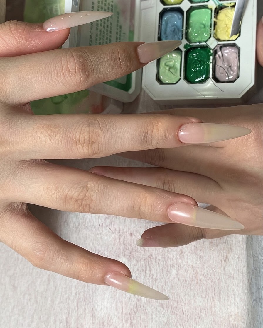 Eine Hand hält einen Schwamm über eine Farbpalette und tupft gelbe Farbe auf eine lange Nagelspitze.