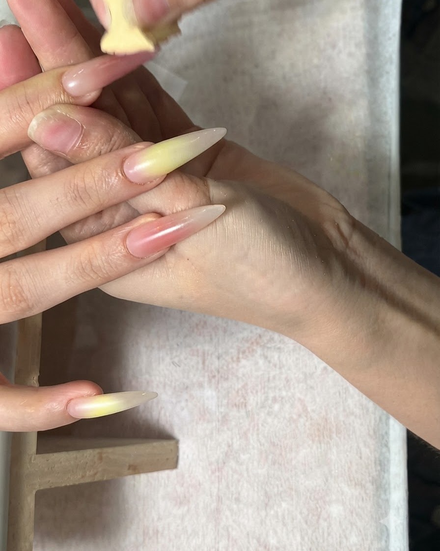Eine Hand, an der mit einem Schwamm Grün- und Korallrot-Töne auf lange Mandelnägel aufgetragen werden.