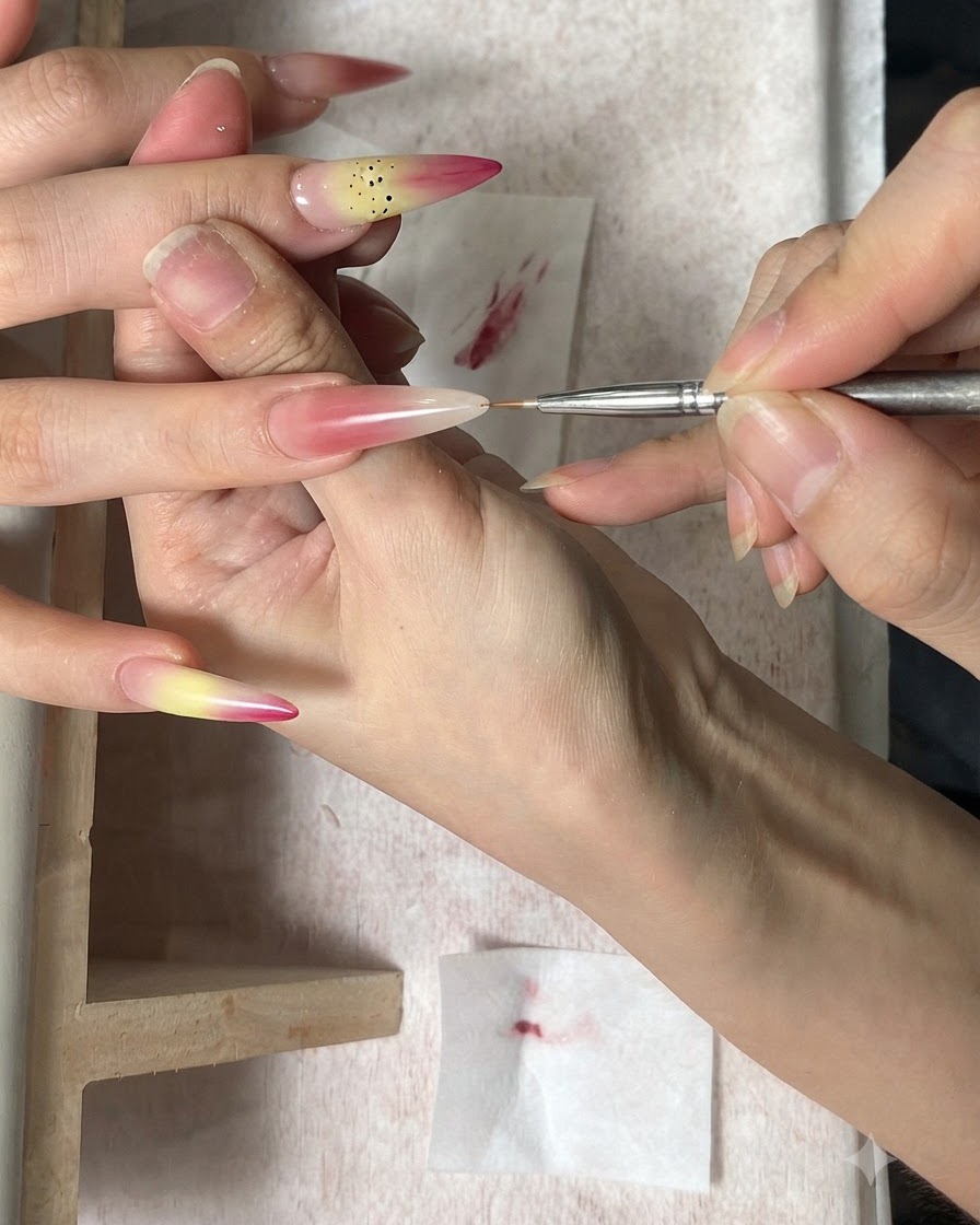 Ein feiner Nailart-Pinsel trägt braune Punkte als Staubblätter auf einen Nagel mit Farbverlauf auf.