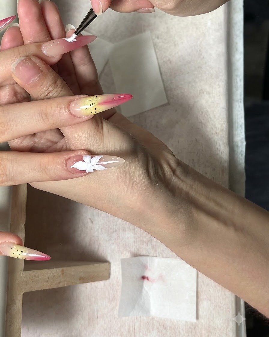 Ein feiner Pinsel malt eine weiße fünfblättrige Blume auf einen länglichen Nude-Nagel.