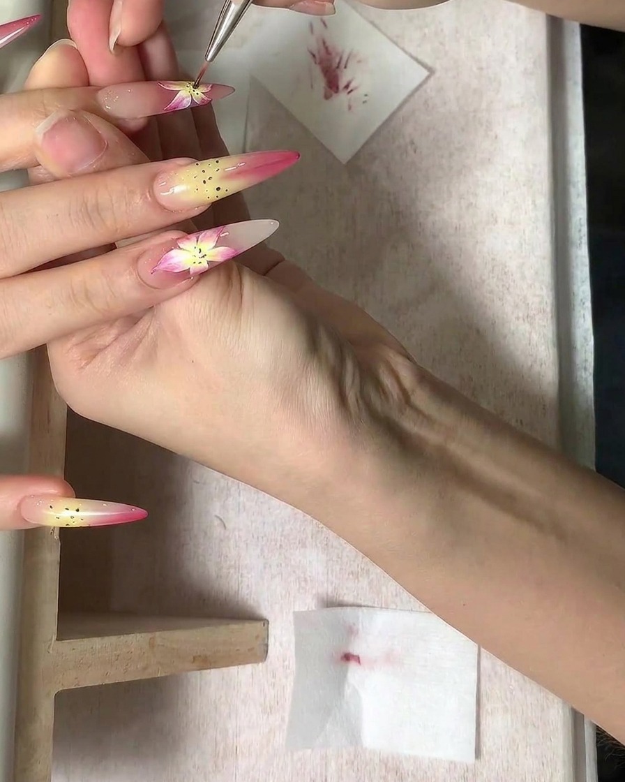 Ein feiner Pinsel fügt detaillierte braune Staubblattpunkte in das Zentrum eines Blumen-Nageldesigns hinzu.
