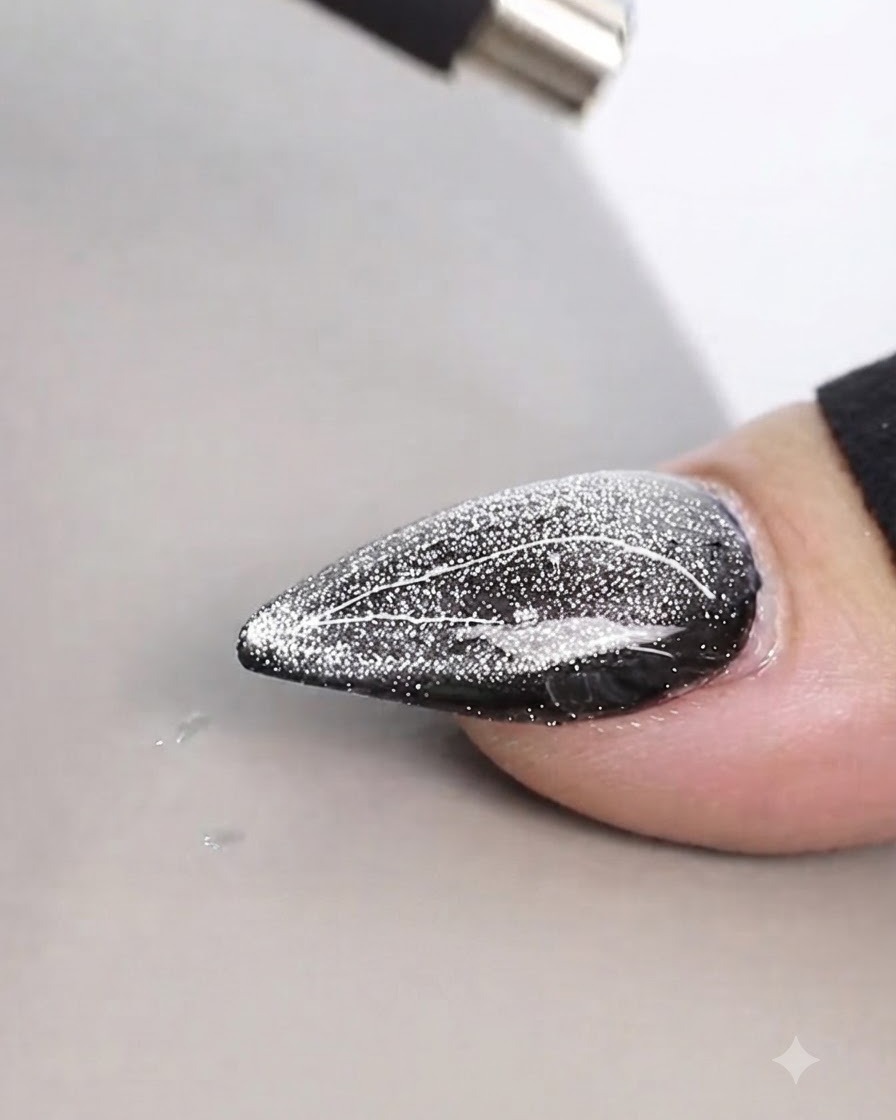Ein zylindrischer Magnet wird dicht über ein schimmerndes Cat-Eye-Nageldesign gehalten, um feine Linien zu erzeugen.