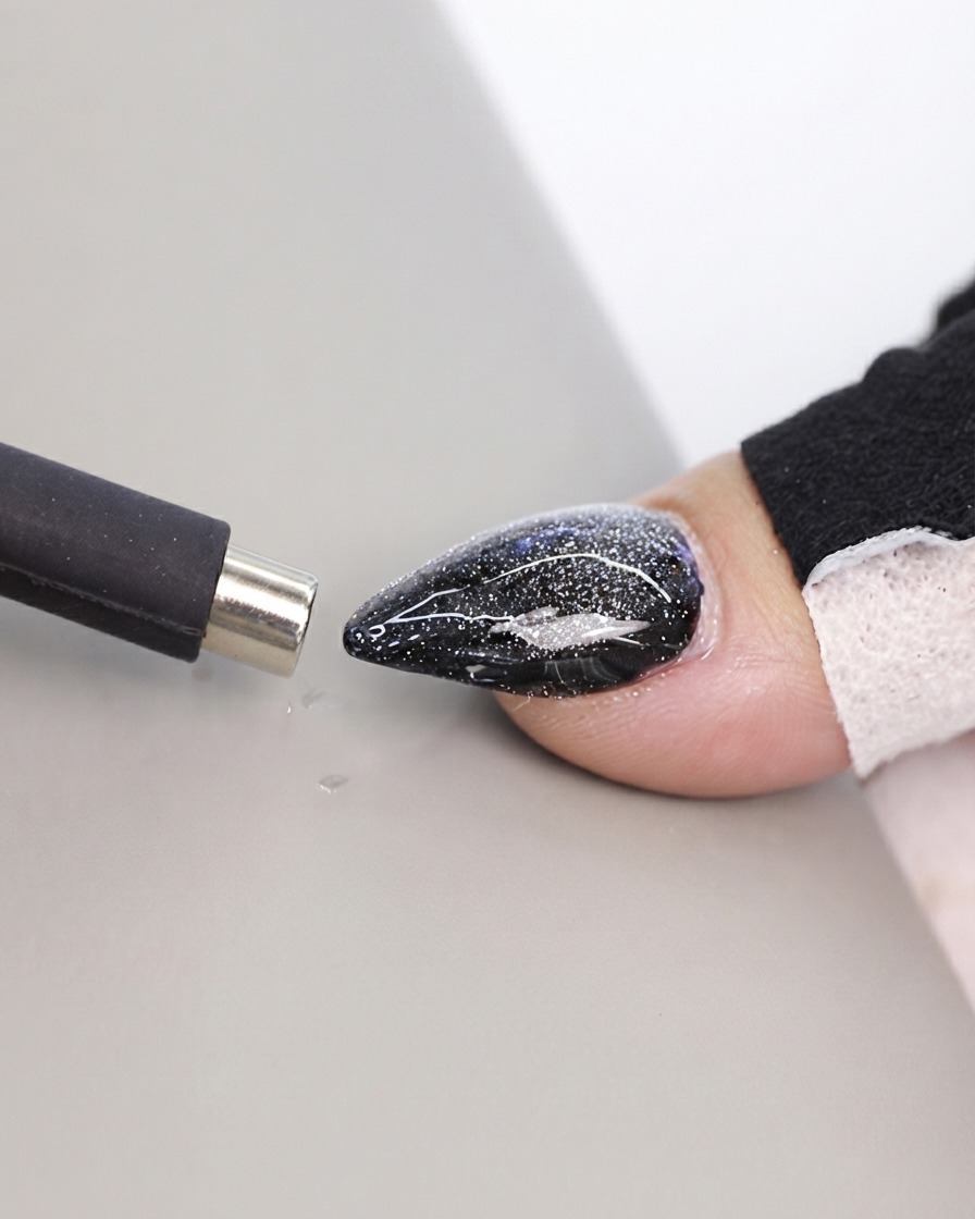 Ein schwarzes Stift-Magnetwerkzeug wird nah an eine strukturierte Cat-Eye-Nageloberfläche herangeführt.