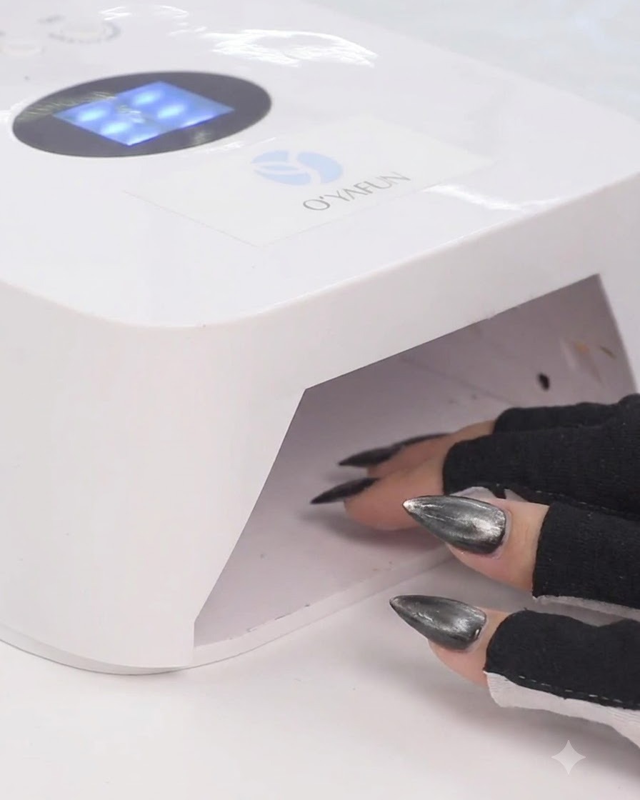 Eine Hand in schwarzen fingerlosen Handschuhen legt Finger in eine weiße UV-LED-Nagellampe, um Gel-Lack auszuhärten.
