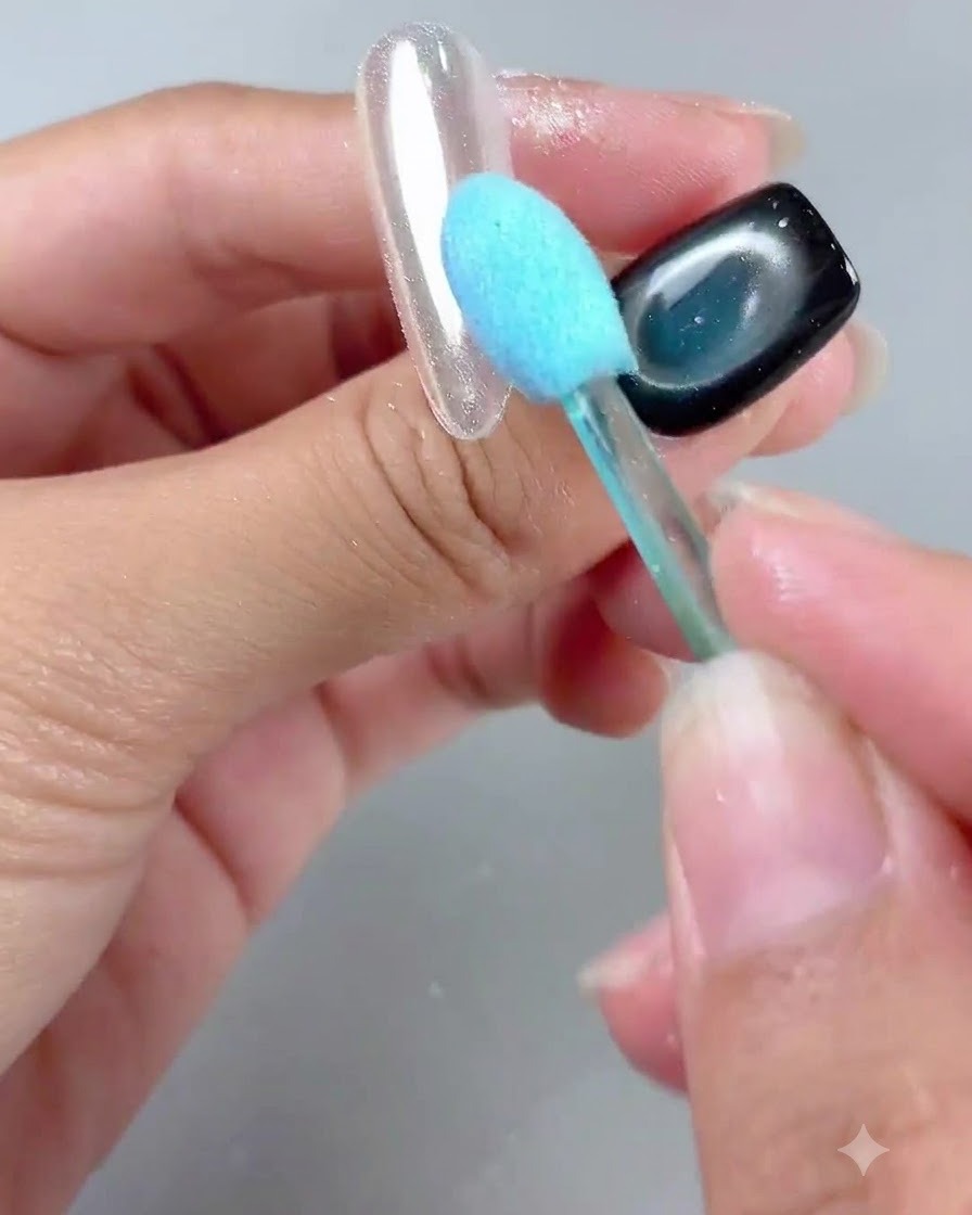 Ein Pinsel mit blauem Griff fegt sanft Puder von einem glänzenden Nageltipp mit Spiegel-Finish.