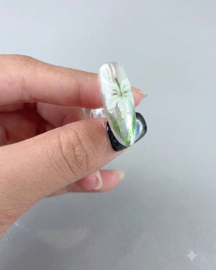 Ein fertiger Nagel zeigt ein weißes Liliendesign unter einer matten Samt-Versiegelungsschicht.