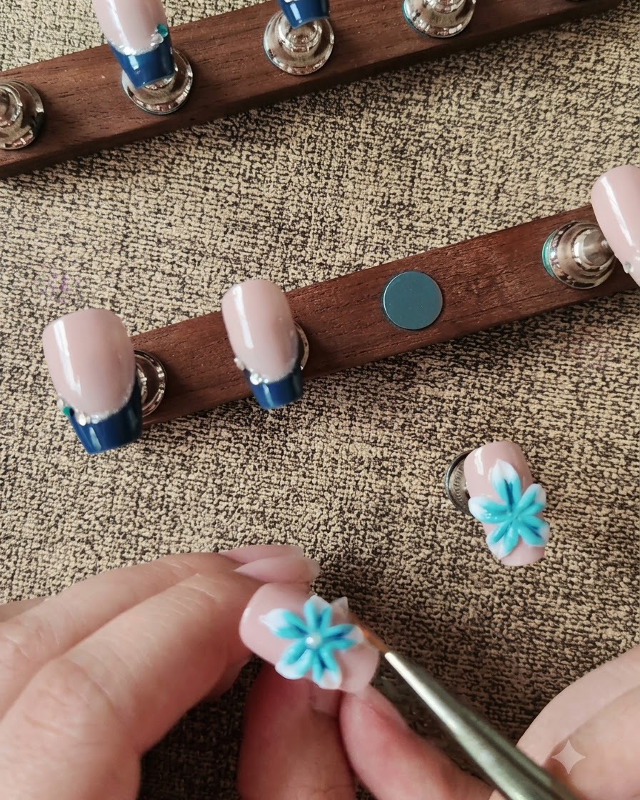 Ein Wachsstift platziert eine weiße Perle in der Mitte einer blau-weißen 3D-Nagelblume.