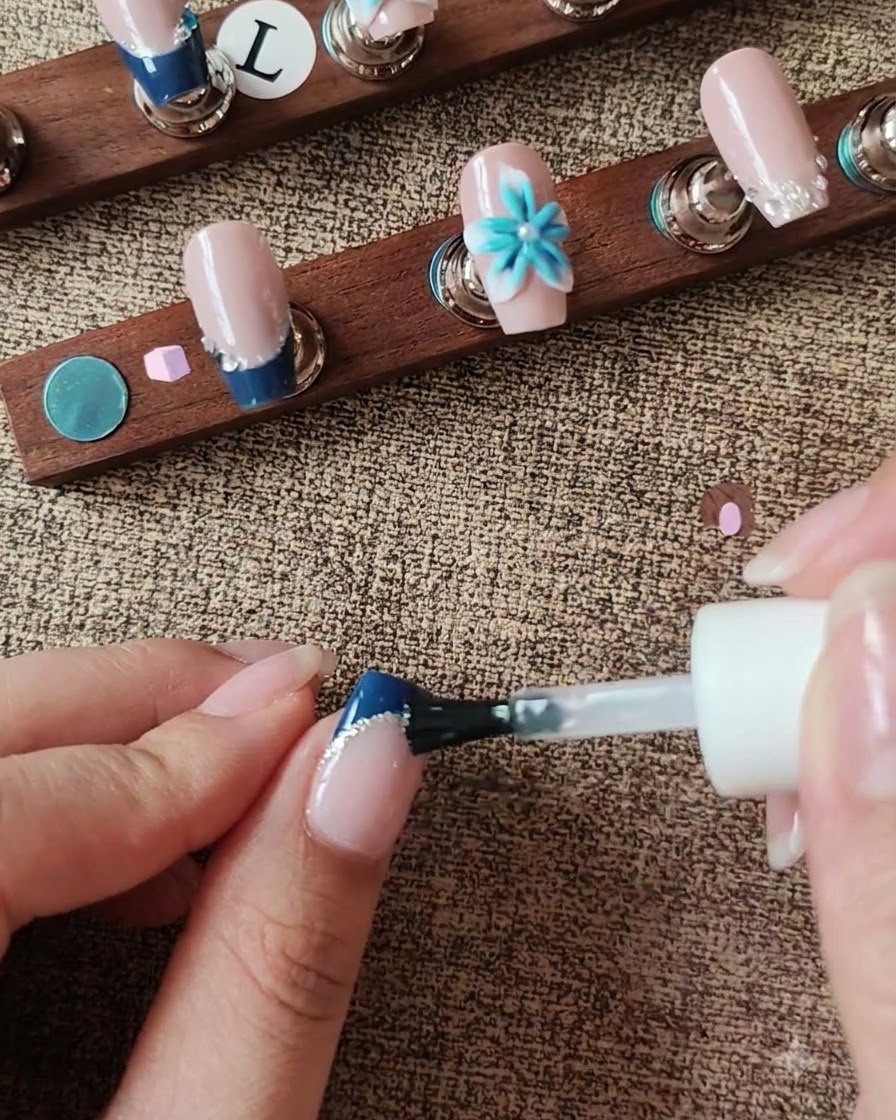 Ein Pinsel trägt Top Coat auf die Nageloberfläche auf und navigiert dabei um einen 3D-Blumenakzent herum.