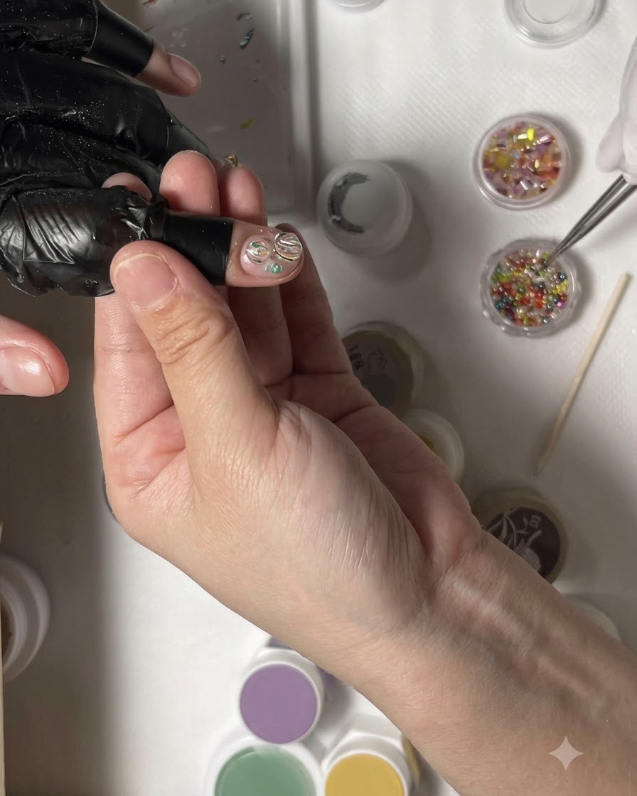 Eine Pinzette platziert einen Cluster winziger, farbiger Strasssteine in der Mitte eines Nageldesigns.