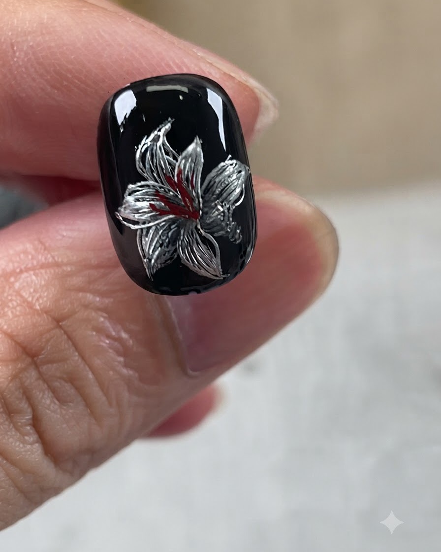 Ein vollendetes Metallic-Lilien-Nageldesign mit schwarzer Basis, silbernen Blütenblättern, weißen Akzenten und roten Zentrumdetails.