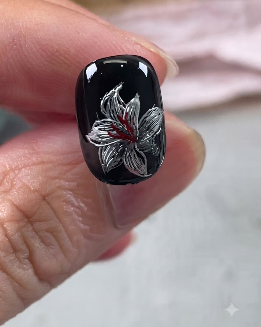 Ein vollendetes Metallic-Lilien-Nageldesign auf schwarzer Basis mit roten und silbernen Details unter einem glänzenden Überzug.