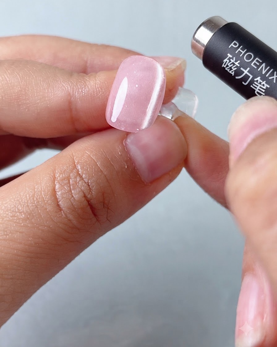 Ein magnetisches Stiftwerkzeug schwebt über einem rosa Cat-Eye-Gel-Nagel, um das Lichtband zu formen.