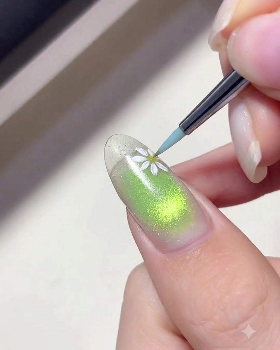 Ein feiner Liner-Pinsel trägt weiße Farbe auf, um zarte Gänseblümchen-Blütenblätter auf einen grünen Nagelhintergrund zu malen.