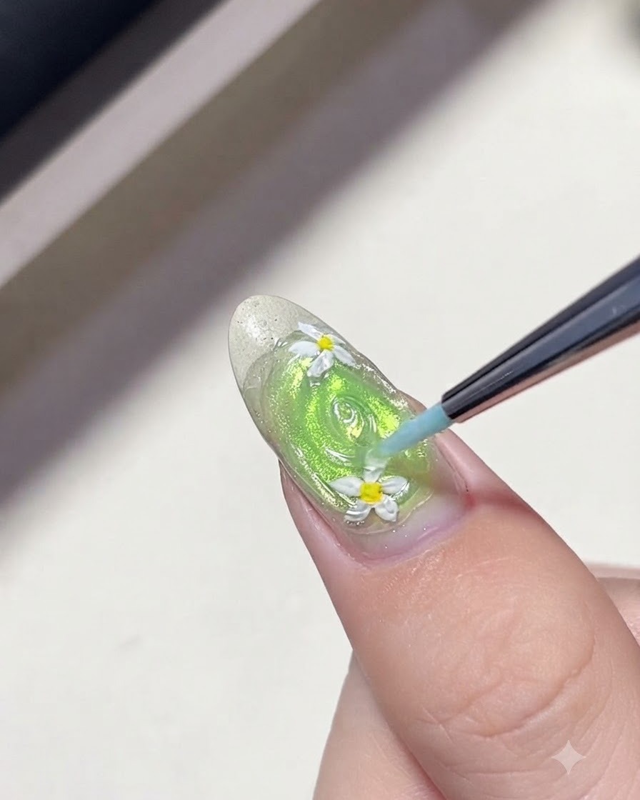 Ein feiner Liner-Pinsel zieht konzentrische Ringe aus klarem Gel um Gänseblümchen auf einem grünen Nagel, um Wasserwellen zu erzeugen.