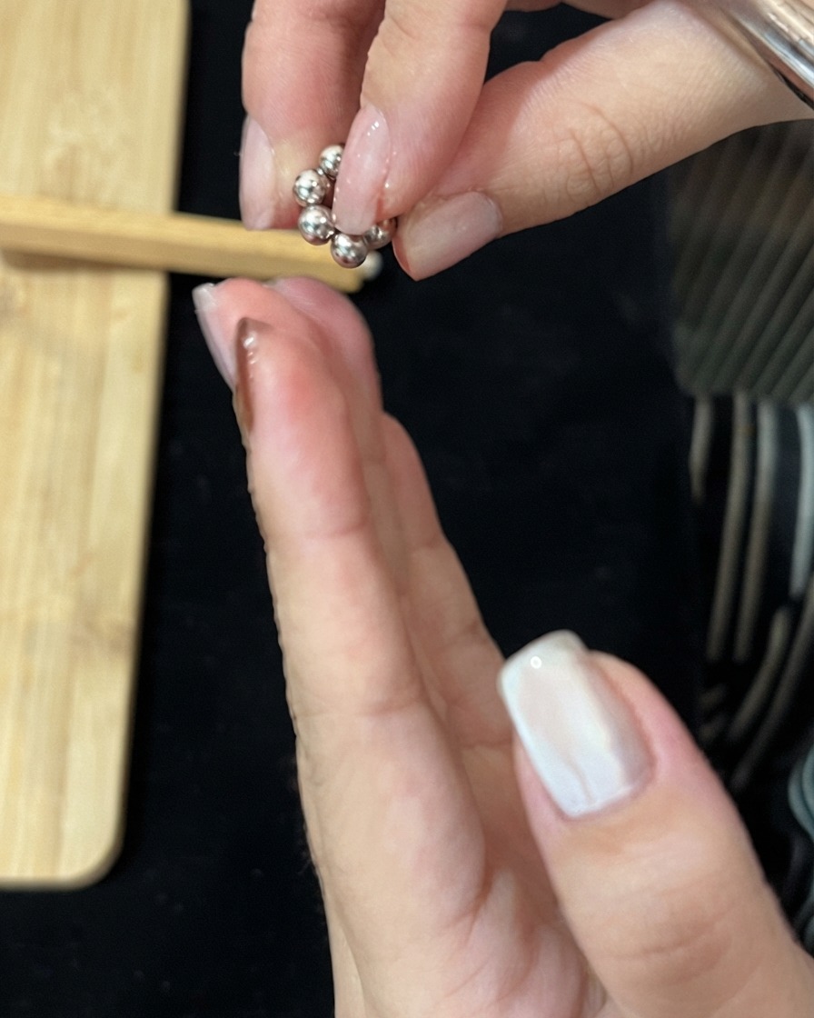 Finger halten eine kleine Ansammlung von metallischen Magnetperlen über eine Hand.
