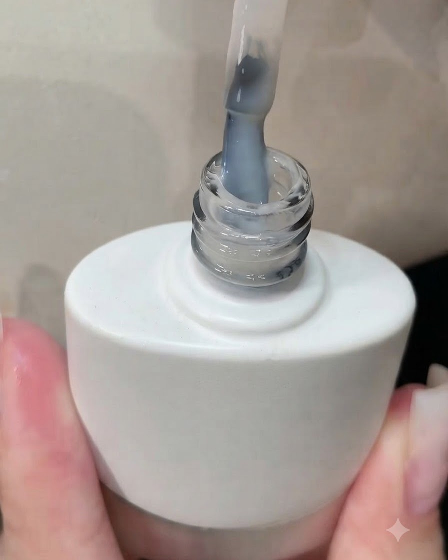 Ein Pinsel wird aus einer Flasche mit weißem Gel-Nagellack gezogen, wobei eine milchig-weiße Schicht auf den Borsten zu sehen ist.