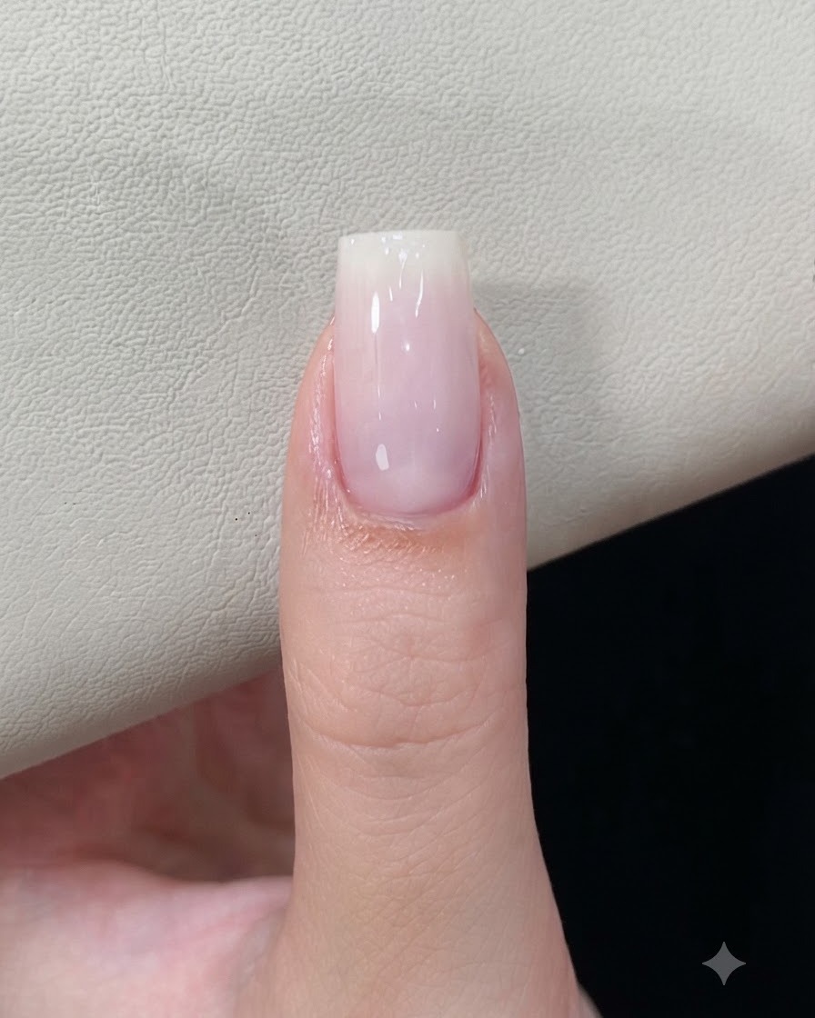 Ein Fingernagel mit einer ausgehärteten milchig-weißen Gelbasis liegt unter einer Nagellampe.