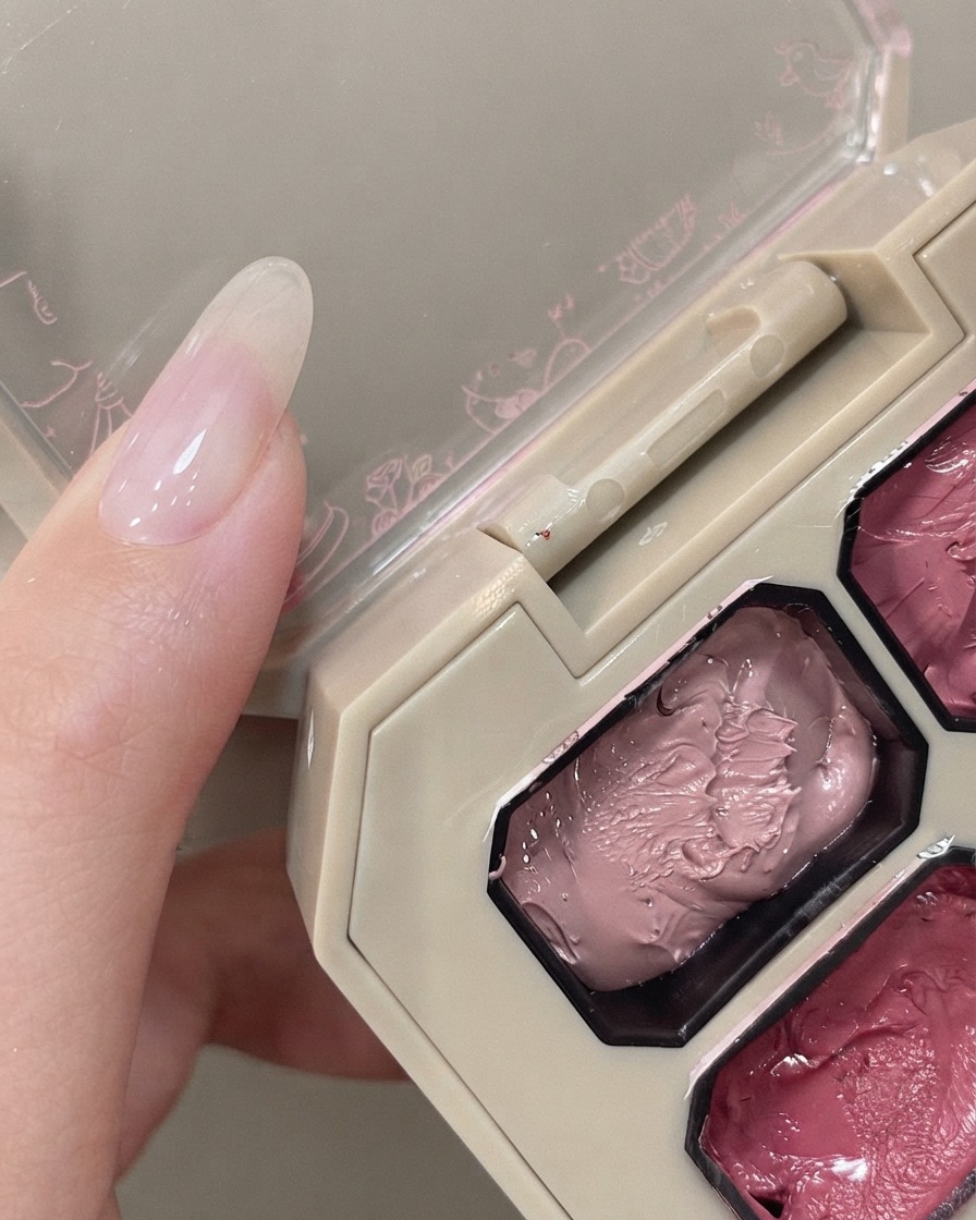 Ein Schwämmchen-Applikator schwebt über einer rosa Pigmentpalette neben einer Hand mit einem Naturnagel.